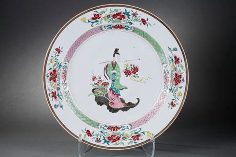 Polychrome : Grand plat en porcelaine de la Famille roseà décor de Magu déesse de la longévité et son panier contenantle champignon lingzhi ( dont est tiré l élixir de longevité ) et la pêche de longévité l ensemble  sur une feuille d'armoise . Elle porte une houe à laquelle est accrochée une branche de pivoineen fleurs - Chine epoque Yongzheng 1723/1735 -
Diam : 43cm