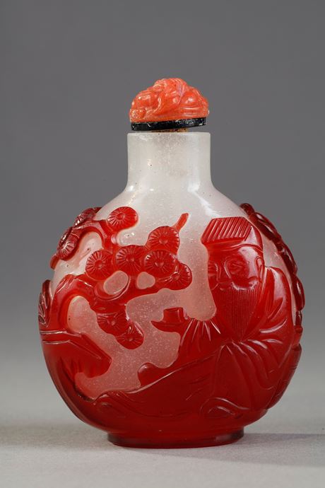Tabatières : Tabatière en verre overlay rouge à decor de Shou Lao tenant une peche de longévité et regardant des peches et sur l autre face d un personnage tenant une tasse sur un plateau devant un pin - Chine 1800/1850