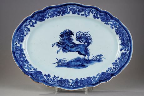 Bleu-Blanc : Grand plat à bord contournés en porcelaine bleu blanc portant un décor d un chien  probablement un epagneul
dressé sur ses pattes arrières sur un sol ou pousse des champignons Lingzi  - Chine epoque Qianlong 1736/1795