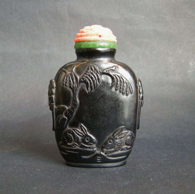 Snuff Bottles : snuff bottle "jais"   sculpted in low relief  with a cat looking a butterfly  and other face with two rabbits . Mask on the sides - 19th century - 