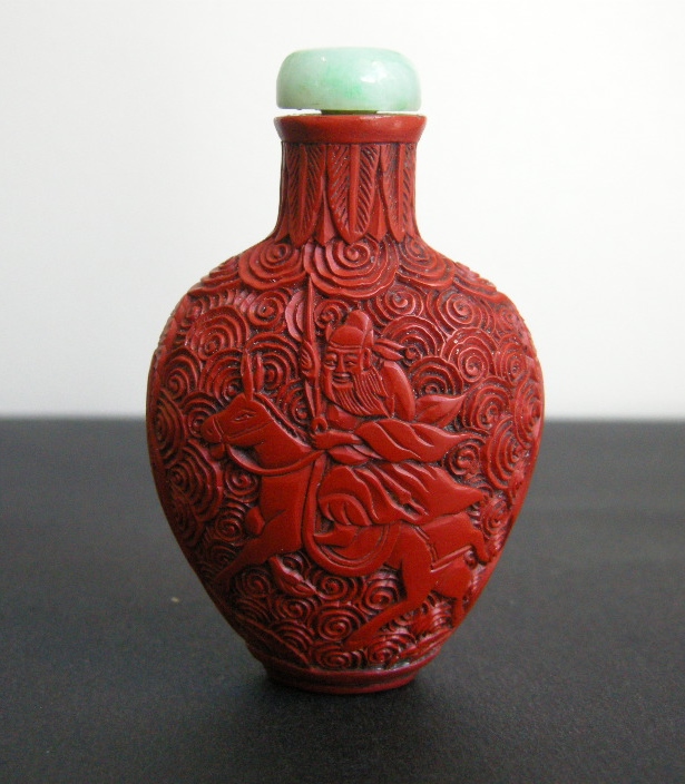 Snuff Bottles : cinnabar lacque snuff bottle on metal decorated and sculpted with a rider on one side and characters on a trolley on the other 
China 19th century
H 6,8 cm