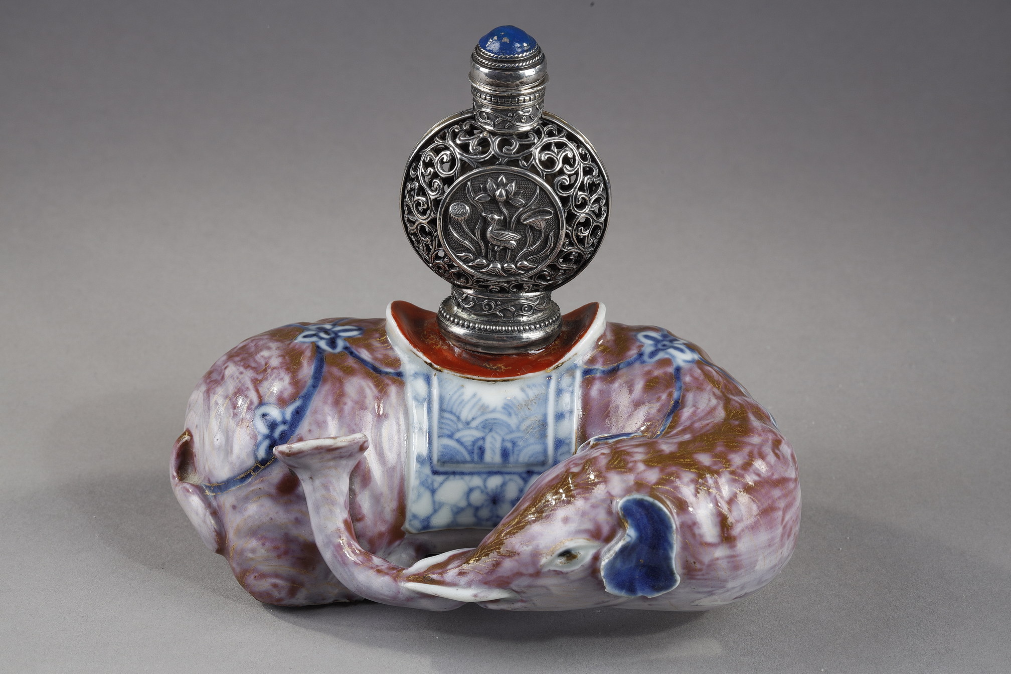 Snuff Bottles : Elephant figure lying in porcelain carrying on its back a silver snuffbottle reticulated in the spirit of Mongolia most probably from the Beijing Imperials workshops and specially adapted for the back of the elephant-
Circa 1790/1820