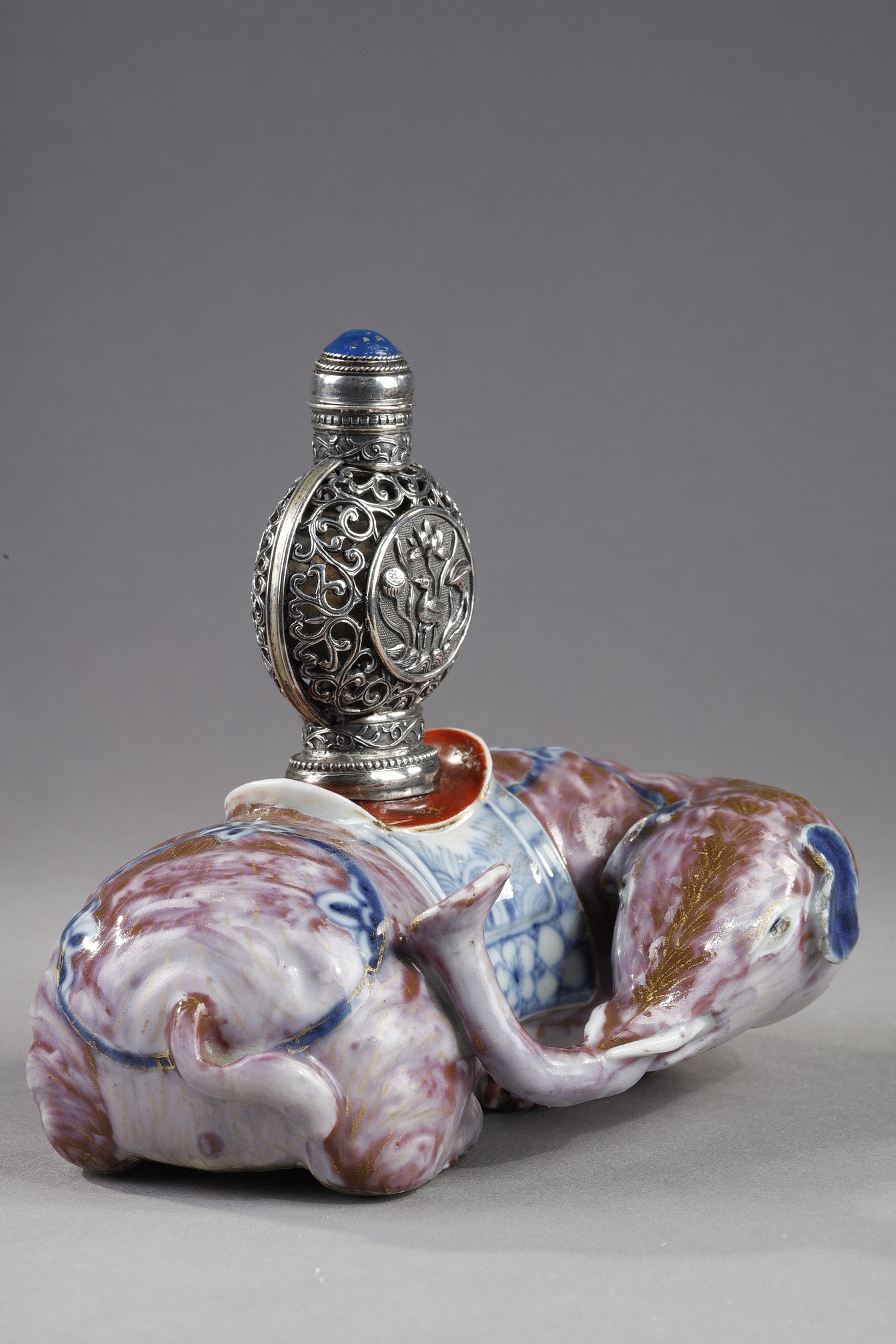 Snuff Bottles : Elephant figure lying in porcelain carrying on its back a silver snuffbottle reticulated in the spirit of Mongolia most probably from the Beijing Imperials workshops and specially adapted for the back of the elephant-
Circa 1790/1820