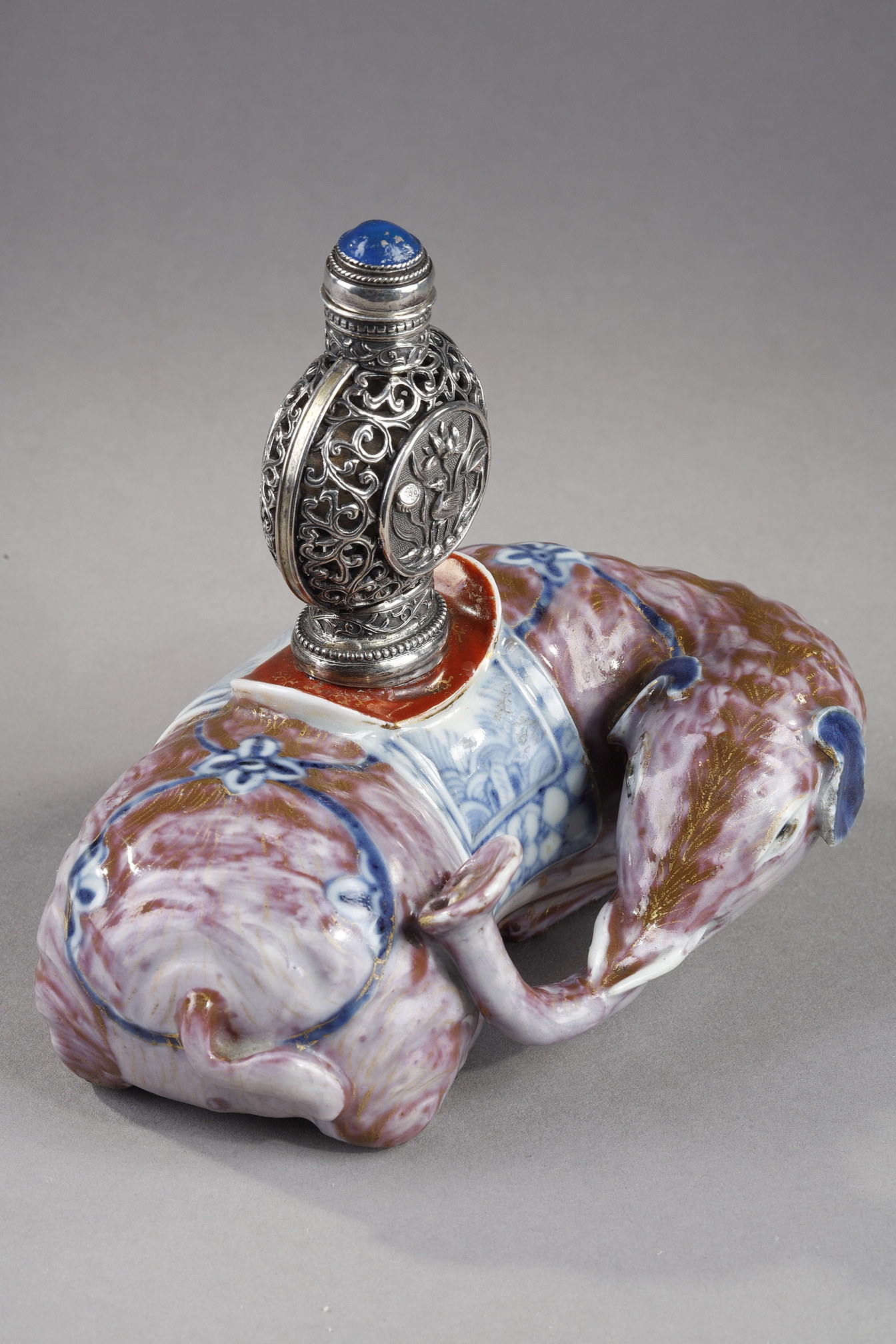 Snuff Bottles : Elephant figure lying in porcelain carrying on its back a silver snuffbottle reticulated in the spirit of Mongolia most probably from the Beijing Imperials workshops and specially adapted for the back of the elephant-
Circa 1790/1820