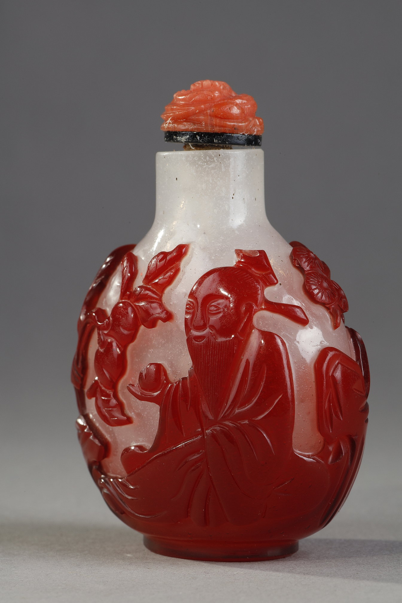 Snuff Bottles : Snuff bottle  red overlay glass with Shou Lao holding a peche of longevity and looking at peches and on the other side of a character holding a cup on a tray in front of a pine - China 1800/1850