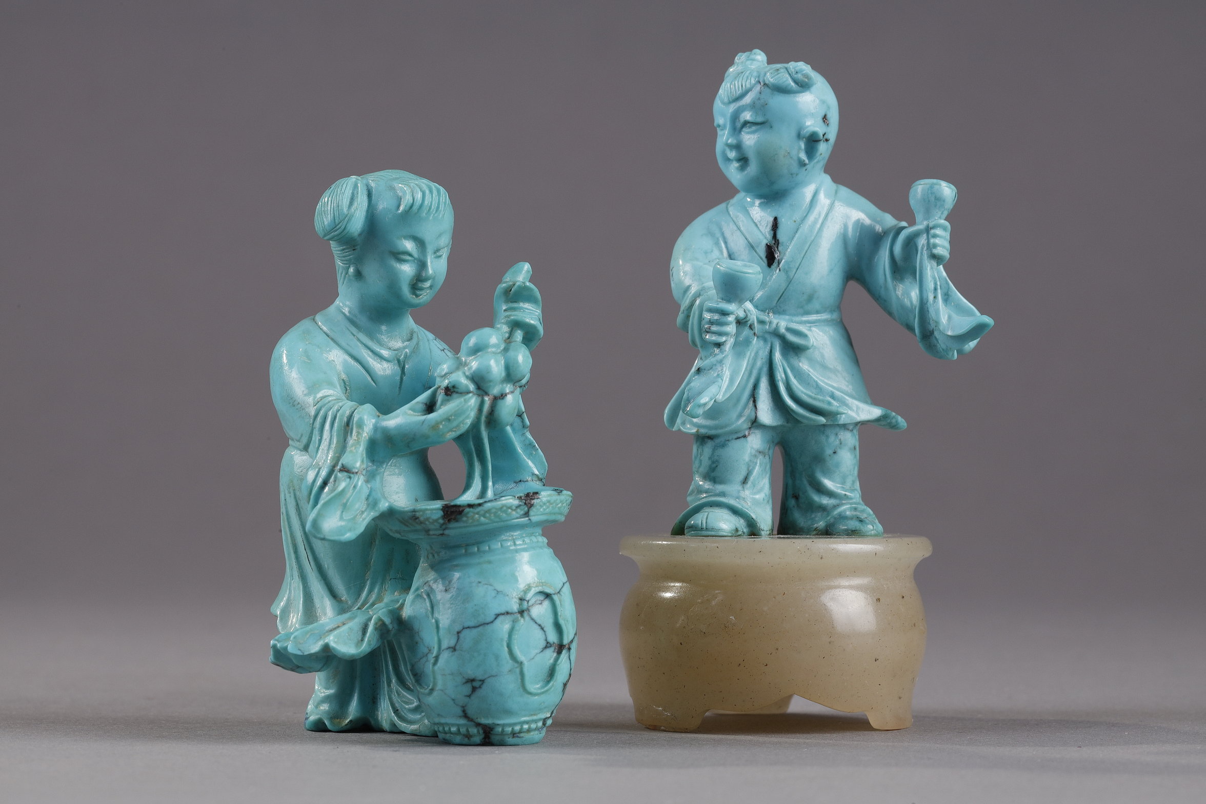 Works of Art : Finely carved turquoise statuettes - China Qing period circa 1900
1)Depicting a young woman pressing fruit on a tray on a barrel-shaped stool 
2) representing a child on a soapstone base 