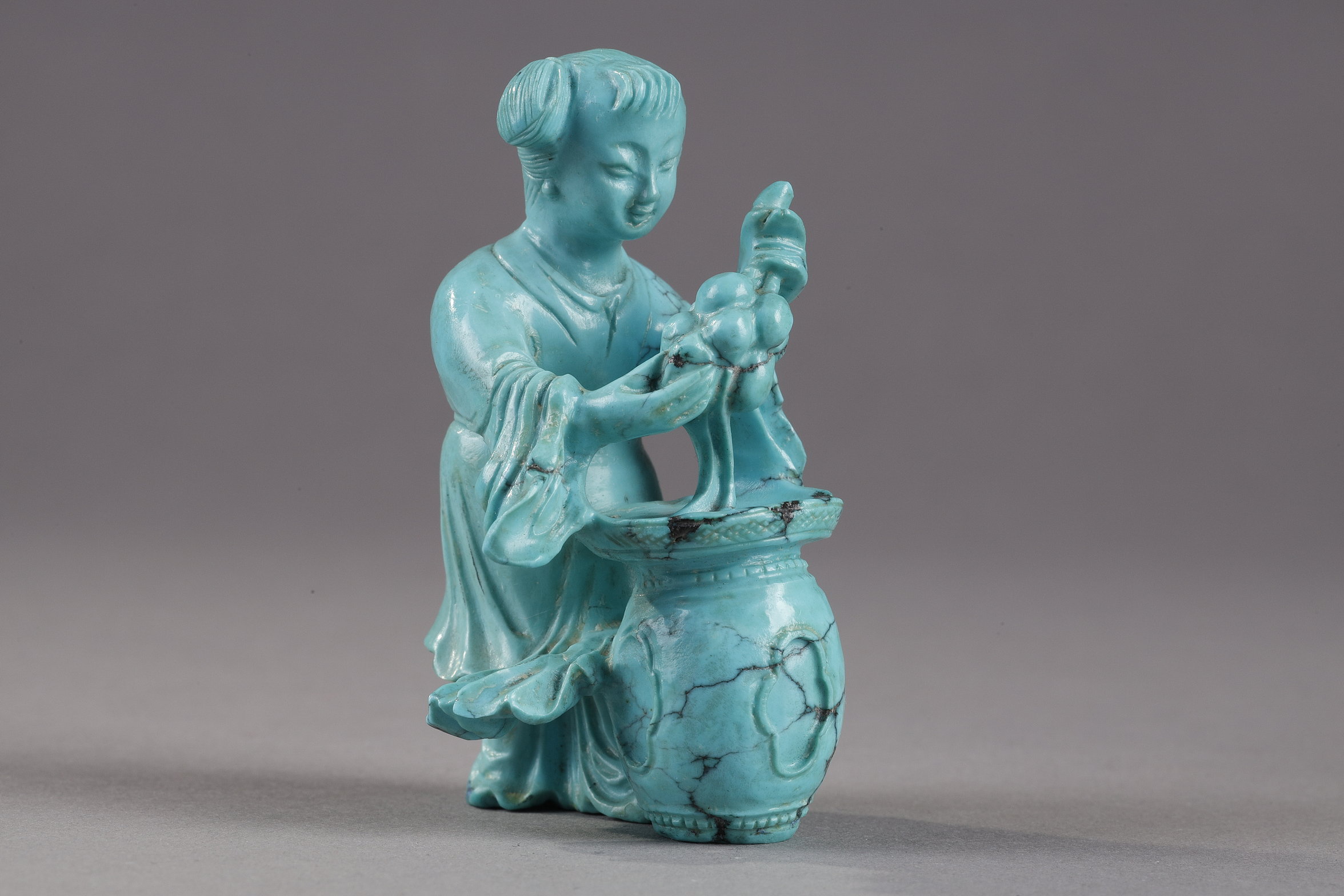Works of Art : Finely carved turquoise statuettes - China Qing period circa 1900
1)Depicting a young woman pressing fruit on a tray on a barrel-shaped stool 
2) representing a child on a soapstone base 