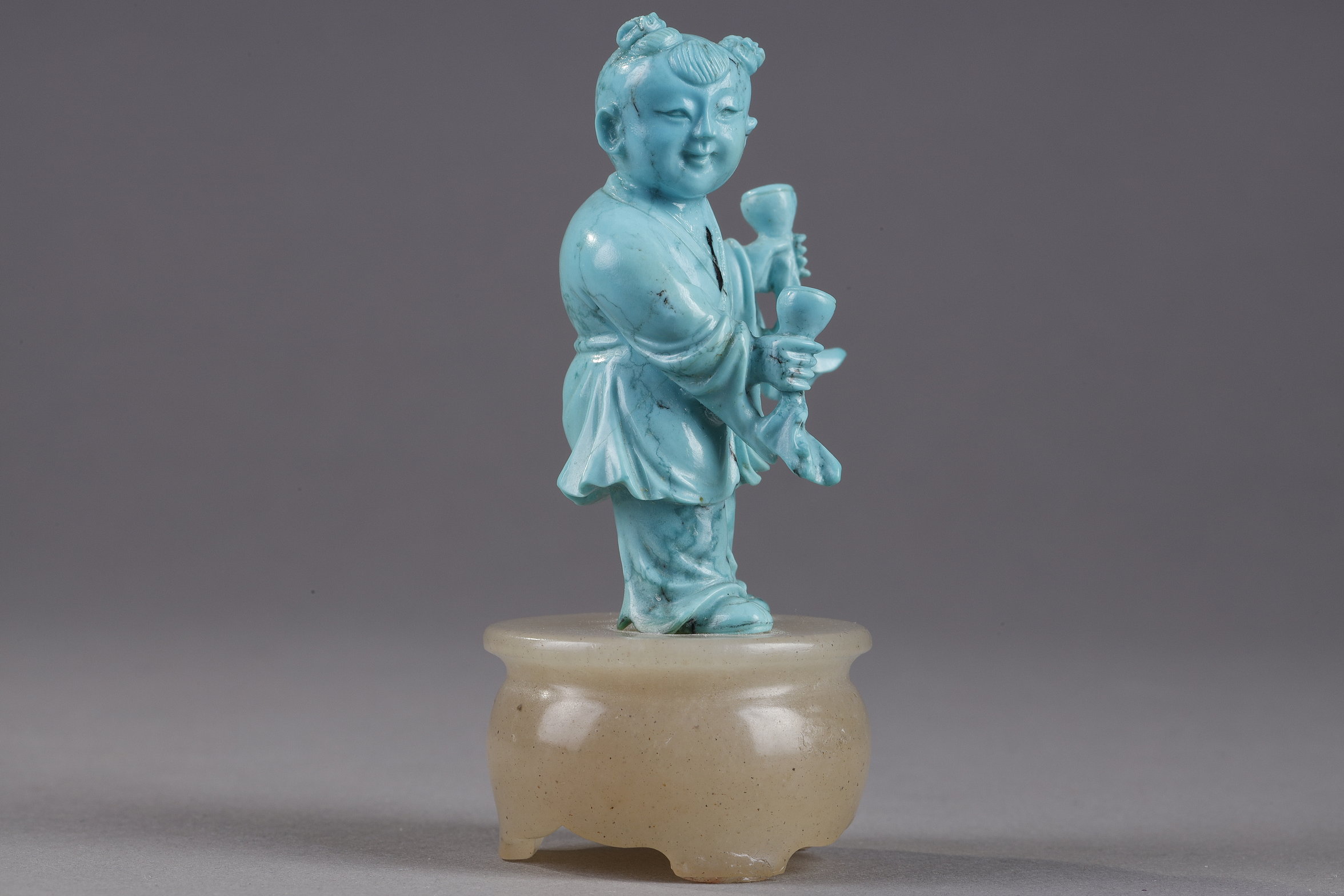 Works of Art : Finely carved turquoise statuettes - China Qing period circa 1900
1)Depicting a young woman pressing fruit on a tray on a barrel-shaped stool 
2) representing a child on a soapstone base 